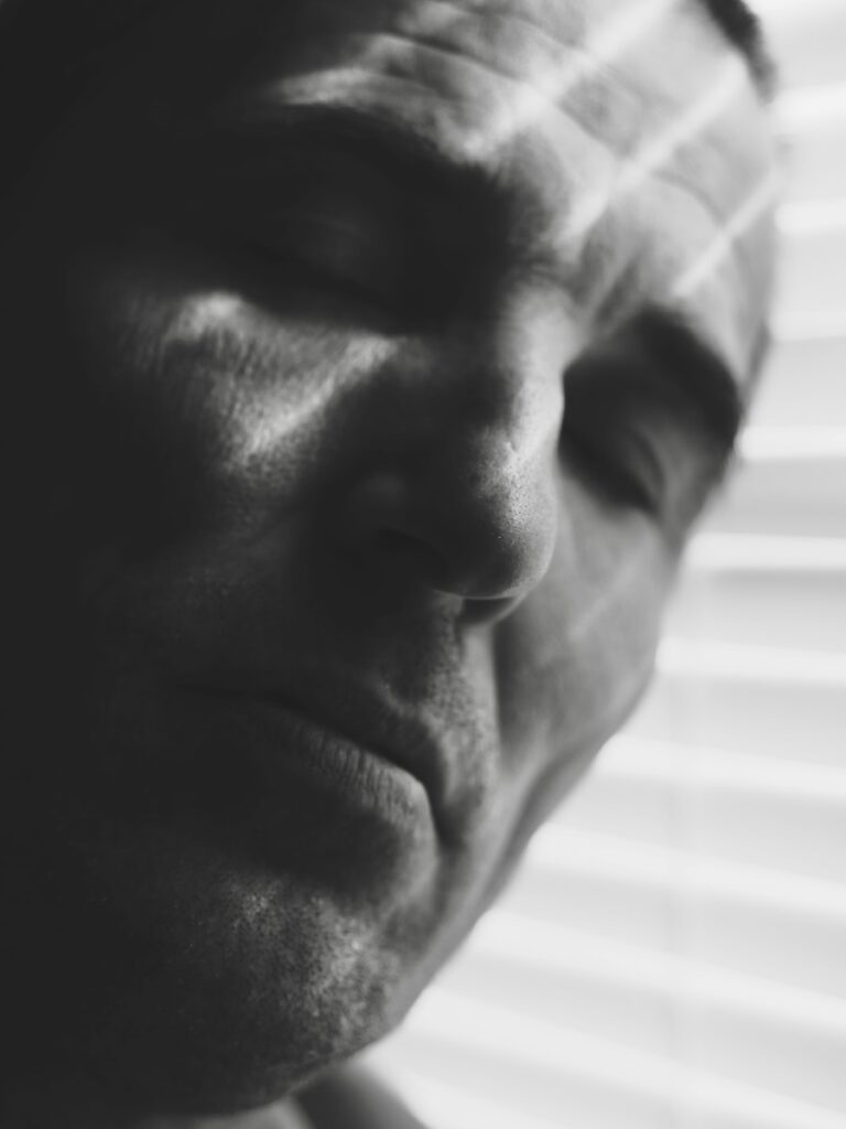 Close-up of a man's face with blinds casting shadows.